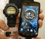 耐久性能の高さを売りにしたタフネススマホ「ＴＯＲＱＵＥＧ０１」は頑丈そうな外観だ。腕時計（左）とも連携する＝８日、東京都内