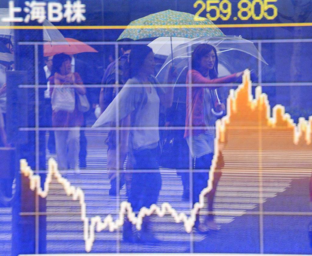 空梅雨が続いていた関東地方にようやく雨が降り、傘を差して街頭を歩く女性らの姿を映した株価ボード＝１１日、東京都中央区（大橋純人撮影）