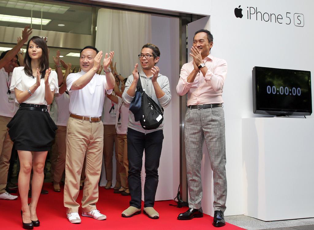 iPhoneの新機種が発売され、ドコモショップで記念セレモニーが開かれた。拍手で発売開始を祝う、（左から）女優の堀北真希さん、ドコモの加藤薫社長、先頭に並んでいた男性、俳優の渡辺謙さん＝２０日午前、東京都千代田区（松本健吾撮影）