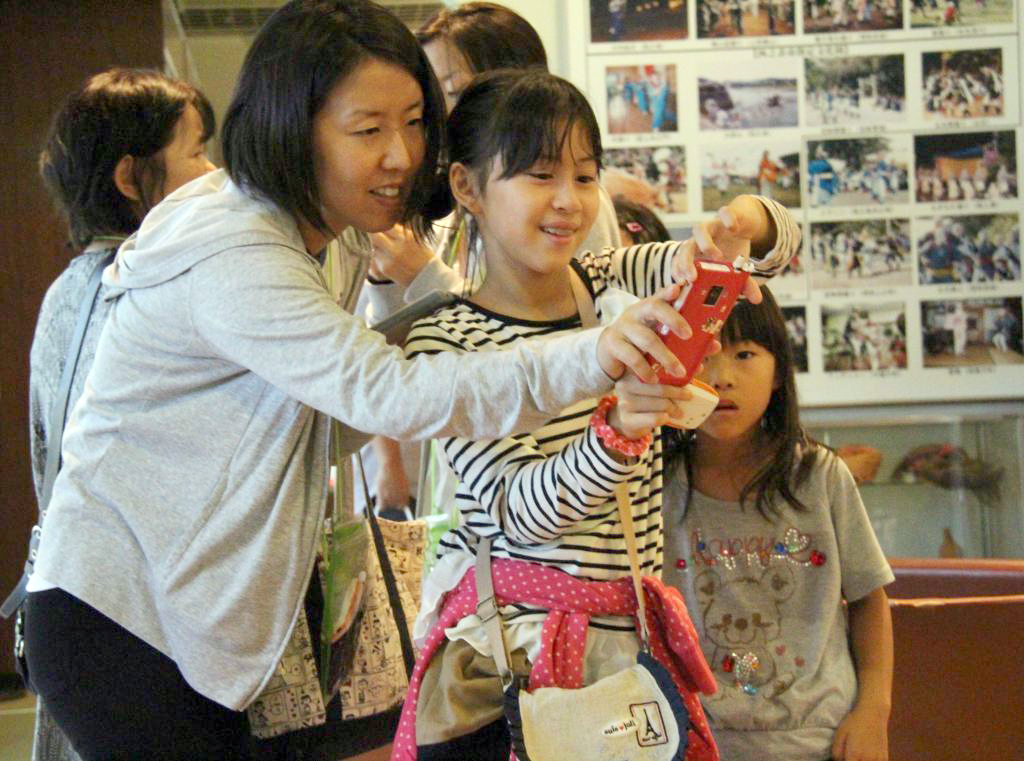 スマートフォンの画面に映るキャラクターの解説を楽しむ参加者＝２６日、種子島