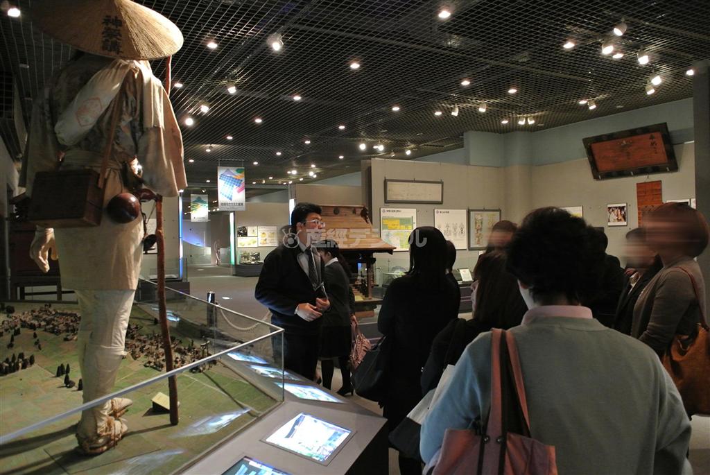 来館者に説明をする富士吉田市歴史民俗博物館の学芸員、布施光敏さん（中央）＝２０１３（平成２５）年１０月３０日、山梨県富士吉田市（中央大学ＦＬＰ深澤ゼミ有志学生記者撮影）。※一部画像を加工しています。