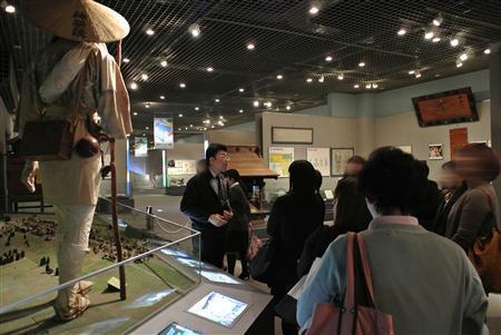 来館者に説明をする富士吉田市歴史民俗博物館の学芸員、布施光敏さん（中央）＝２０１３（平成２５）年１０月３０日、山梨県富士吉田市（中央大学ＦＬＰ深澤ゼミ有志学生記者撮影）。※一部画像を加工しています。