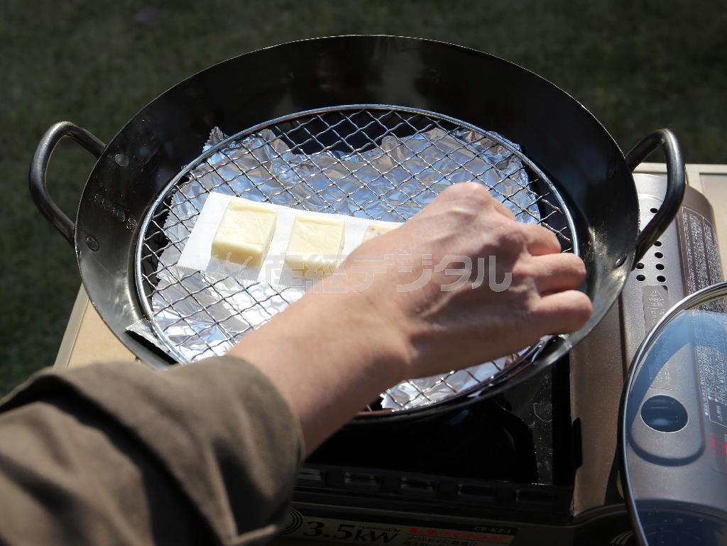 （手順３）食材を並べる。★ポイント１＝チーズの場合は、熱で溶けて網から落ちてしまうため、クッキングシートを敷いておく。カマンベールチーズはアルミホイルでトレーを作ってその上に乗せる。★ポイント２＝複数の食材を同時に燻製してもいいが、匂いが混ざるのを防ぐため魚と肉など匂いの強いもの同士はＮＧ。★ポイント３＝タラコは最初から入れると火が通りすぎてしまうため、煙が出てから入れる（宮崎裕士撮影）