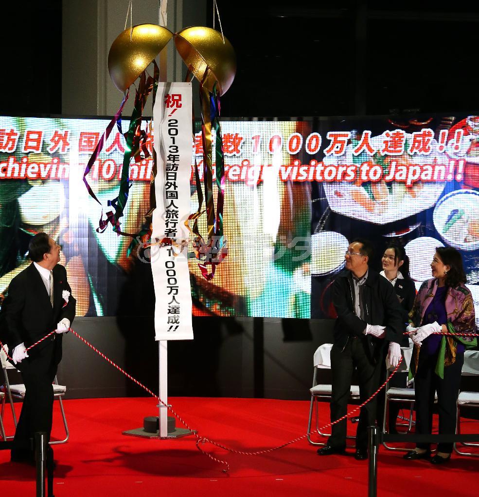 訪日外国人旅行者数１０００万人達成の記念セレモニーで、太田昭宏国土交通相（左）とくす玉を割るタイから来たパパン・パッタラプラーシットさんと妻のユパーダー・パッタラプラーシットさん＝２０１３年１２月２０日、千葉県成田市・成田空港（小野淳一撮影）