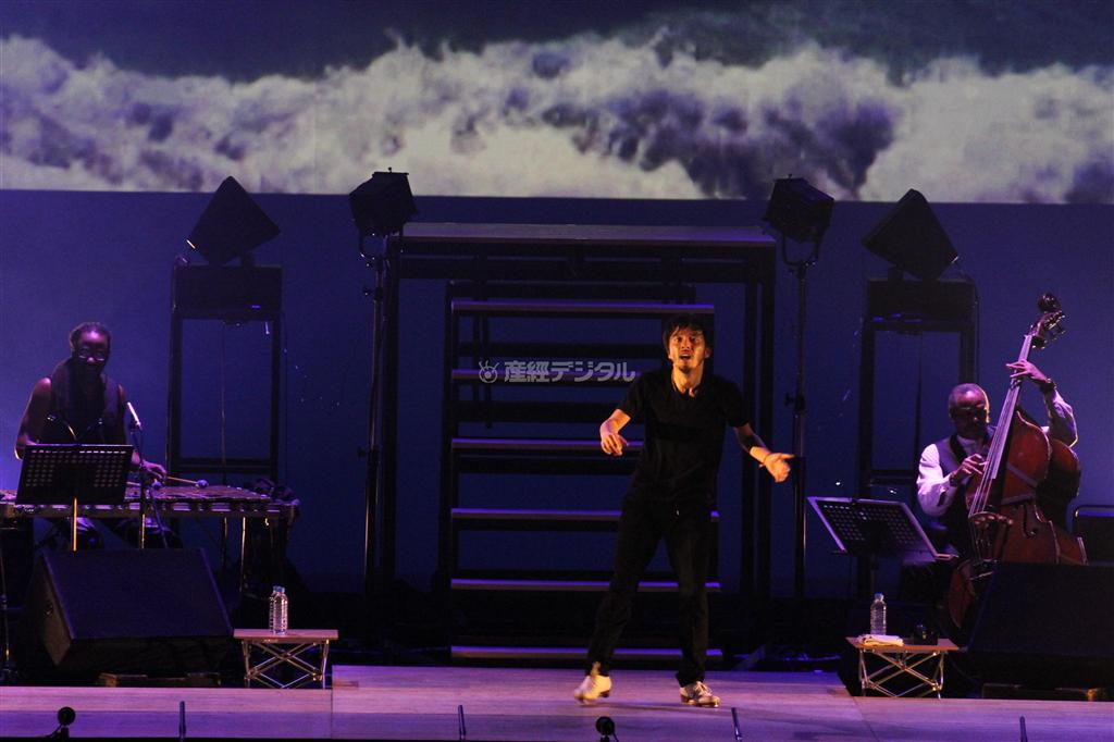 今回の凱旋公演のインスピレーションを得ようと足を運んだんＮＹ州最東端の街、モントークの映像をバックにタップを踏む熊谷和徳さん。ベースやビブラフォンなどと掛け合いを演じながら音楽を完成させた＝２０１４年１月１８日、東京・渋谷のＢｕｎｋａｍｕｒａオーチャードホール（田中幸美撮影）