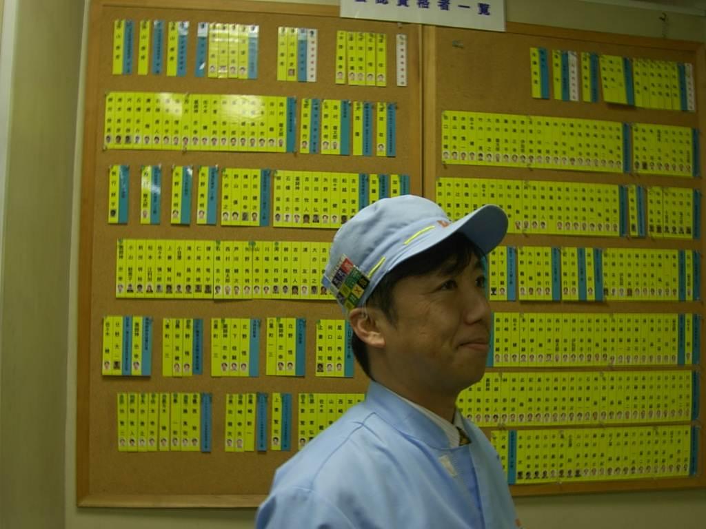 フジキンの工場内に張り出された資格取得者の一覧表と帽子に付けたバッジ。資格取得者に手当てを支給し、奨励する（同社提供）