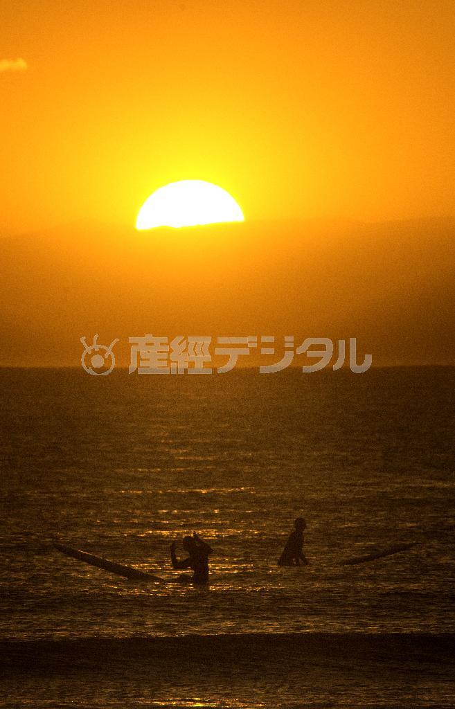 晴れたかと思うと低く黒い雲が垂れ込め、雲間に沈む夕日が冬のサーファーを照らす＝２０１４年１月２６日、神奈川県鎌倉市・材黙座海岸（渡辺照明撮影）