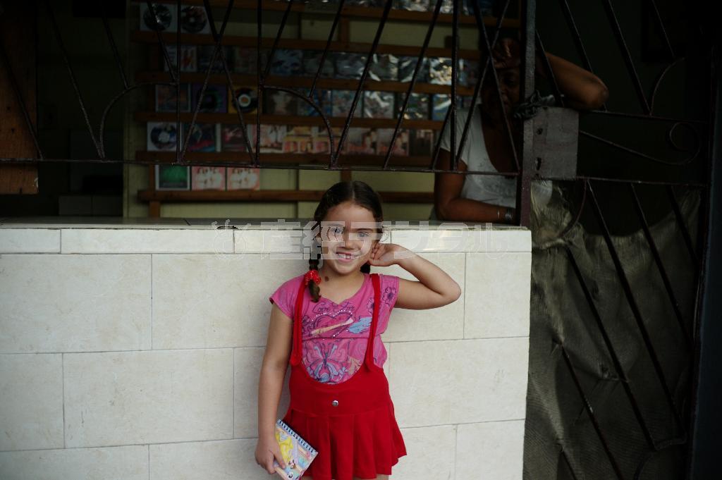 首都ハバナの街角で、三つ編みがかわいらしい女の子を見つけてぱしゃり。後ろにいるＣＤ屋の女性も興味深そうに見つめる＝キューバ（緑川真実さん撮影）