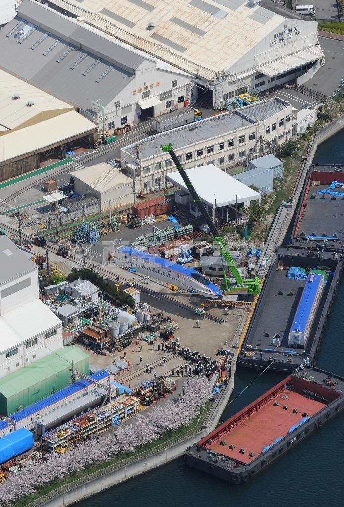 クレーンで台船に積み込まれる北陸新幹線用新型車両Ｗ７系＝７日午前１１時６分、神戸市兵庫区（本社ヘリから、大塚聡彦撮影）