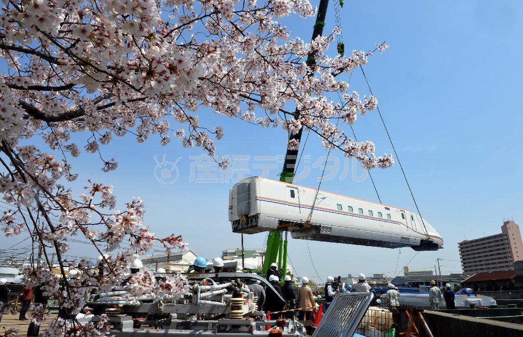クレーンでつり上げられ工場から搬出される北陸新幹線新型車両Ｗ７系＝７日午前１１時７分、神戸市兵庫区の川崎重工業兵庫工場（頼光和弘撮影）