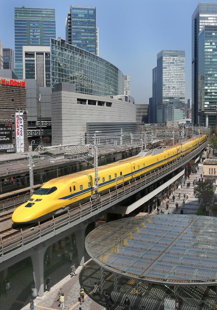 東京駅を出発、西へ向かうドクターイエロー。黄色い車体が都心のビル街に映える＝東京・有楽町