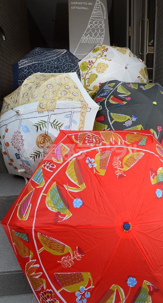 手前のプリント折りたたみ雨傘（７８００円）の生地は手染めではなく機械によるが「重色」の風合いは再現され、ぬくもりが漂う。日傘（中の白、２万円）の柄は刺繍