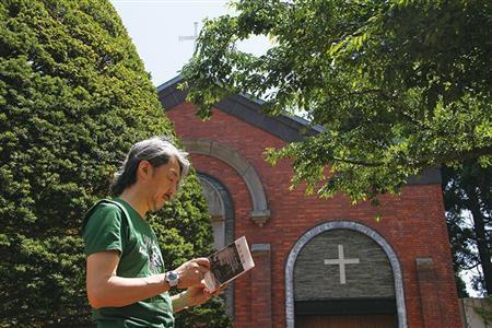 函館のトラピスト修道院の庭で、自著『僕の音、僕の庭』を手にする井上鑑。この静かな風情の奥に、実に自在な音楽力とすこぶるラディカルな思考が秘められている＝北海道・函館市（小森康仁さん撮影、松岡正剛事務所提供）