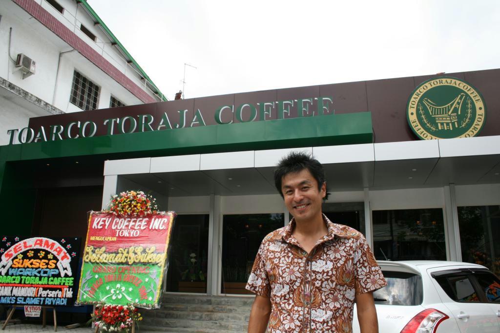 キーコーヒーの直営カフェ「トアルコトラジャコーヒーショップ」と、トアルコ・ジャヤの中野正崇副社長＝８日、インドネシア・マカッサル