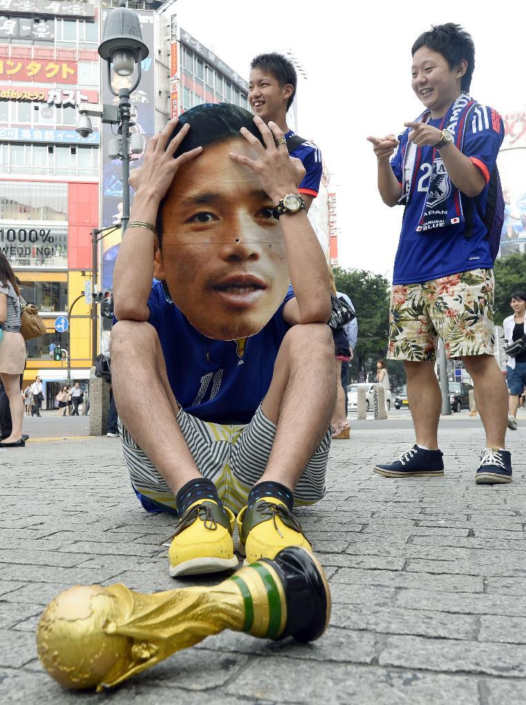 日本の１次リーグ敗退が決まり、東京・渋谷の路上で頭を抱え座り込む日本代表・長友選手のお面をつけたサポーター＝２５日朝