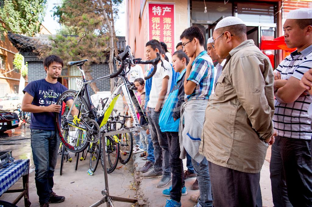 レース後にバイクのメンテナンスをするチームスタッフと、その様子を興味津々に見守る回族の人たち＝２０１４年７月１２日、中国・青海省（田中苑子さん撮影）