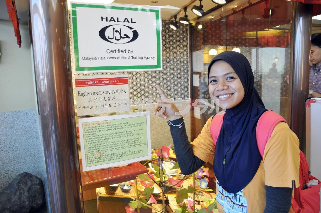 成田空港の天ぷら店で、イスラム教徒向け料理を示す「ハラル」マークを指さすインドネシア人旅行者クスマさん＝２０１４年８月２日、千葉県成田市（共同）