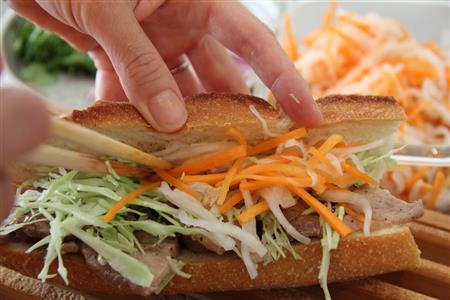 バインミー（ベトナムのサンドイッチ、作り方２）＿＿バゲットにバターを塗り、（作り方１：調理した豚肉）をのせて粗びきこしょうをふり、キャベツ、紫たまねぎ、なます、香菜をのせて挟む（田中幸美撮影）