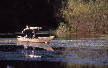 オモロチカに乗り銃を構える。流れの緩い支流で舟の中でシカを待つという＝ロシア・クラスヌイ・ヤール村（伊藤健次さん撮影）
