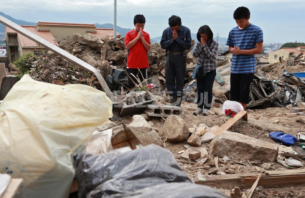 亡くなった近所の人に花を手向け、手を合わせる家族＝２０１４年９月２０日、広島県広島市安佐南区八木（松永渉平撮影）
