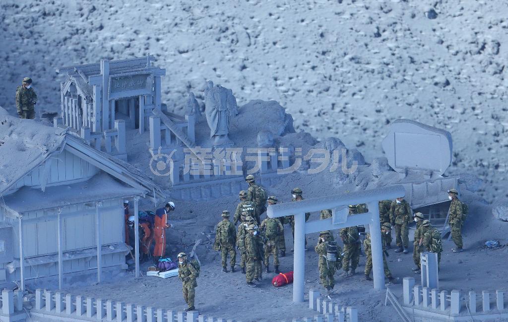 御嶽山（おんたけさん、３０６７メートル）の山頂にある御嶽神社付近で捜索活動を行う自衛隊と消防の捜索隊。噴火によって社殿は火山灰に覆われ、ご祭神の像も首が折れてしまった＝２０１４年９月２８日午前（本社チャーターヘリから、大山文兄撮影）