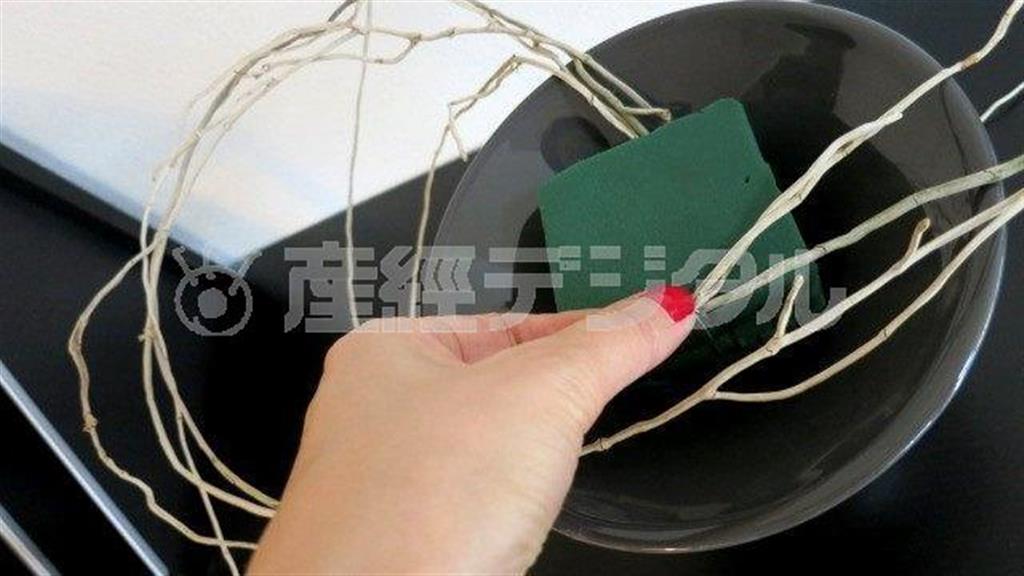 （手順１）花器にカットしたオアシスをセットし、ランの根っこを挿し、花器から離れるようなフォルムで動きをだしてＵピンでとめる＝２０１４年９月１９日（花千代さん提供）