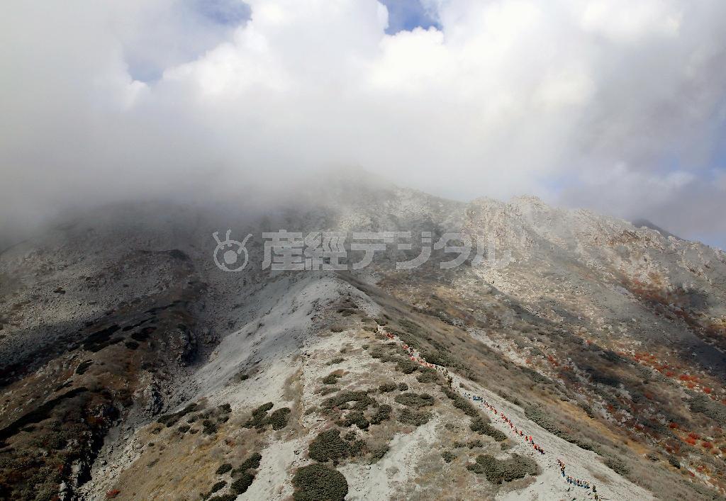 噴煙と雲に覆われた御嶽山（おんたけさん、３０６７メートル）山頂に向け、登山道を登る警察、消防、自衛隊の隊員ら（右下から中央）＝２０１４年１０月２日午前９時４７分（共同通信社ヘリから撮影）