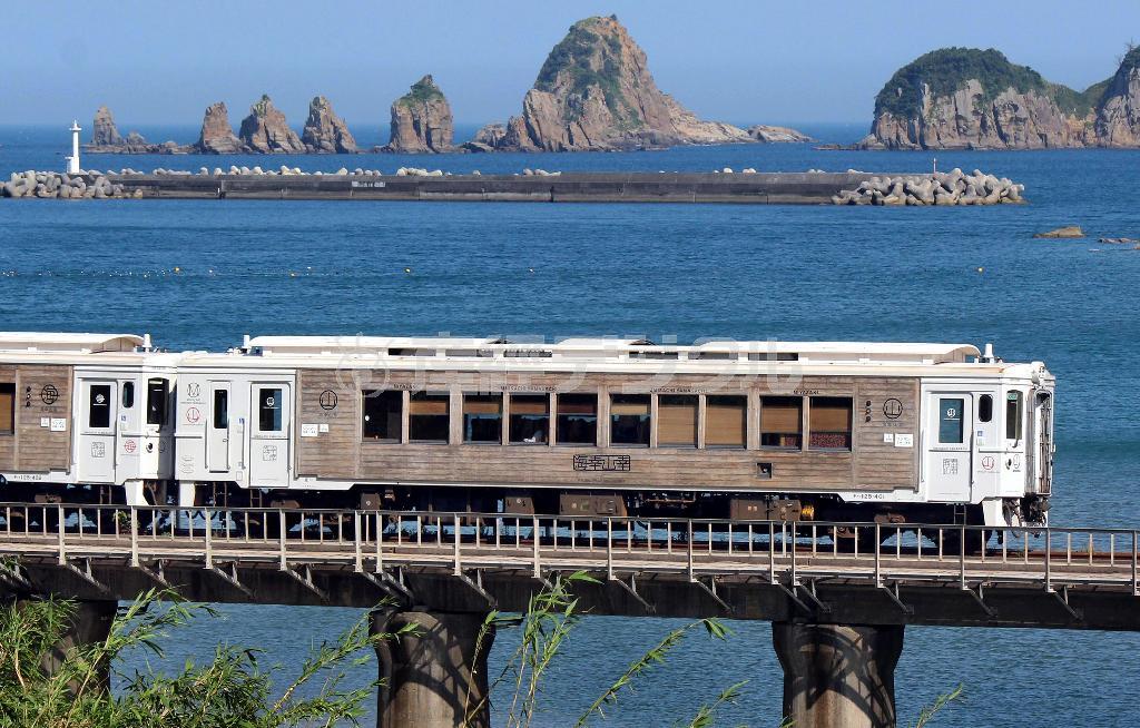 宮崎－南郷を走る「海幸山幸」。車両には地元特産の飫肥（おび）杉が使われている。後方には日南海岸の名所、七ッ岩が見える＝２０１４年７月２６日、宮崎県日南市（鈴木健児撮影）