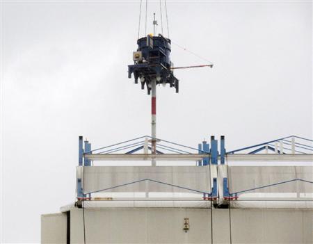 クレーンでつり下ろした機器で、原子炉の建屋カバーの屋根部分に穴を開ける作業。上部のタンクに飛散防止剤が入っている＝２２日午前、福島第１原発１号機（東京電力提供）