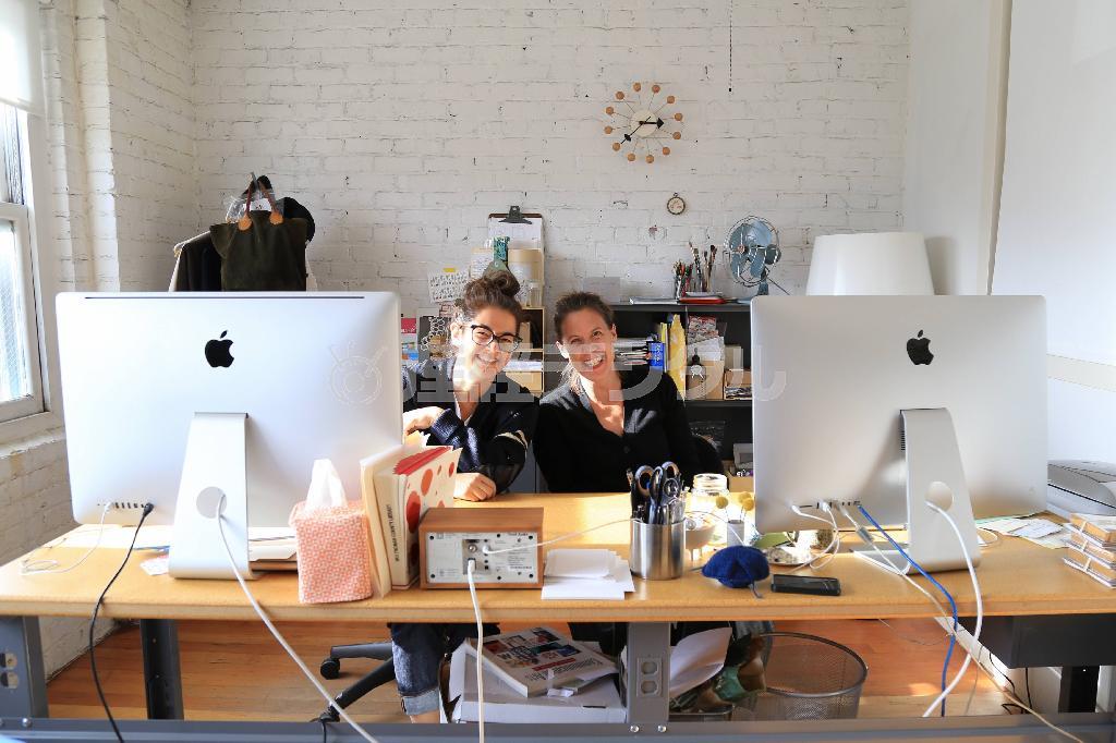 マックの大きなモニターが２つ並んだ机で仲良く写真に納まるプリント工房「エッグ・プレス」取締役のテス・ダーロウさん（右）とデザイナーのキャラ・ヤナガワさん。デザインのプロセスは現代風だが、すぐそばでレトロな活版印刷機が「カッシャンカッシャン」と音をたて、昔ながらの印刷が行われている＝２０１４年１０月２０日、米オレゴン州ポートランド（緑川真実さん撮影）