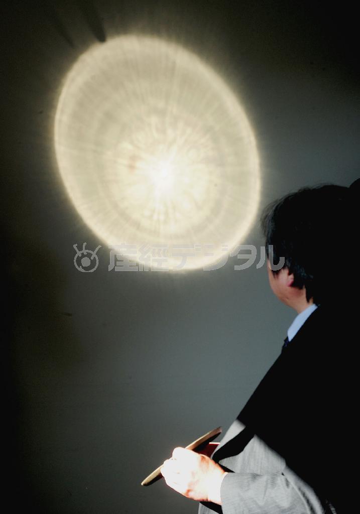 レプリカの三角縁神獣鏡（男性の手元）から投影された反射光。裏面の文様の突起部などが浮かび上がった＝２０１４年１月、京都市東山区・京都国立博物館（共同）