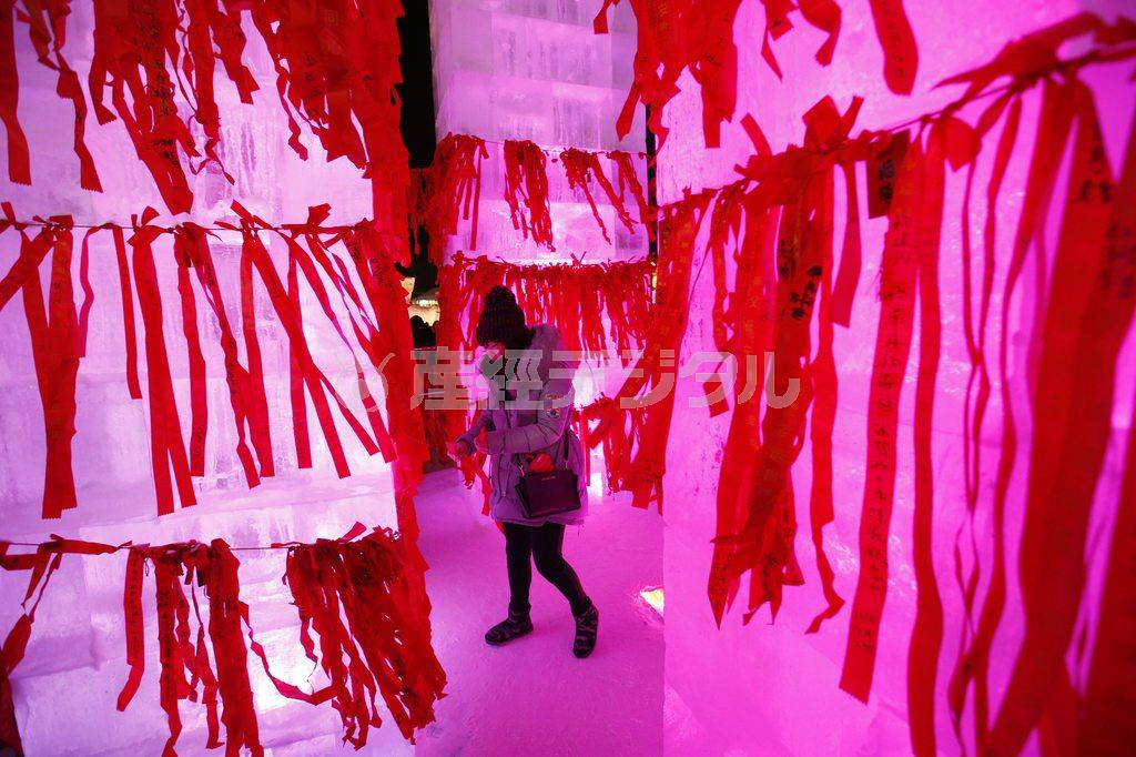 氷でできたお寺の中で願い事を書いた赤いリボンをかける場所を探す女性＝２０１５年１月５日、中国・黒竜江省ハルビン（ロイター）
