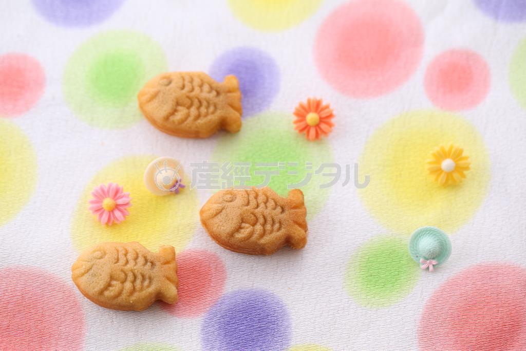 ポップな色合いの布にかわいらしい形のボタンをちりばめて撮ってみました。背景を変えることで同じお菓子がさまざまな顔を見せてくれます。（須藤夕子さん撮影）。※お菓子：梅林堂の満願成就