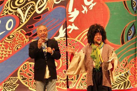 横９メートル、縦５メートルの巨大な自作の幕をバックに、書家の俵越山さん（右）と掛け合いでトークショーをする木村英輝さん＝２０１５年１月１２日、京都市上京区の京都府立文化芸術会館（田中幸美撮影）