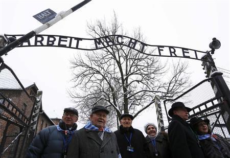 追悼式典に合わせ、アウシュビッツ強制収容所跡を訪れた元収容者ら。当時の囚人服と同じ水色と白の縞模様の布切れを身につけ、「働けば自由になる」と書かれた看板の下を歩いた＝２０１５年１月２７日、ポーランド・オシフィエンチム（ロイター）