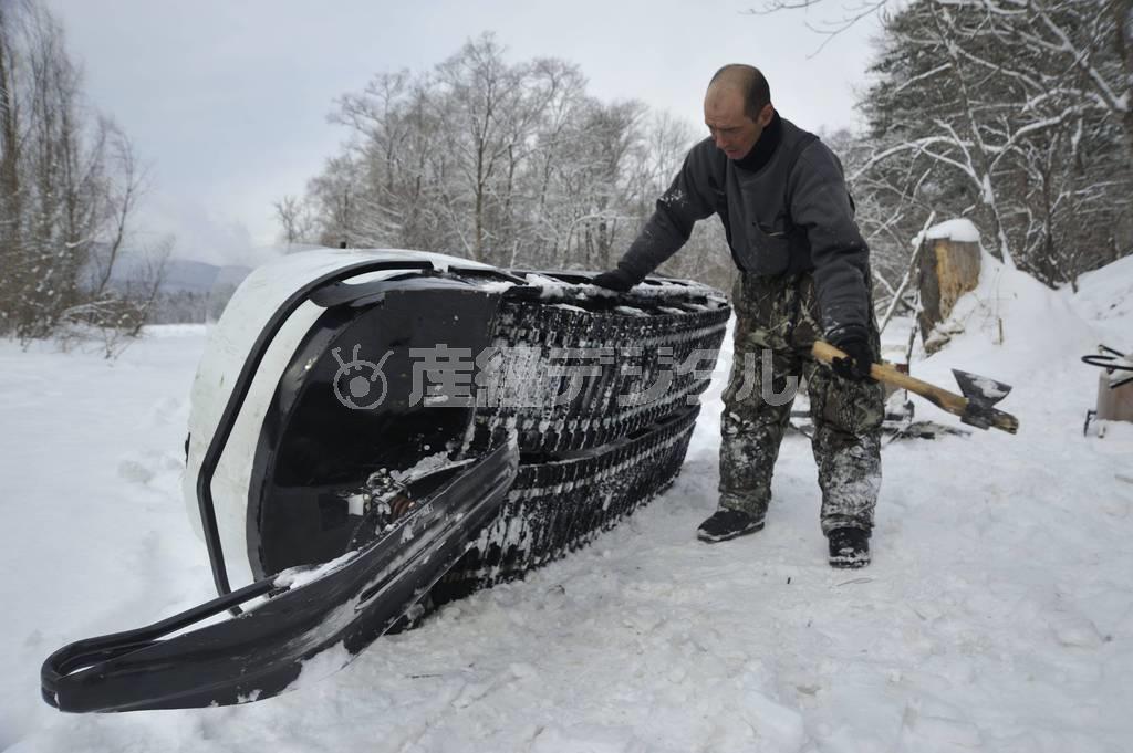 キャタピラについた氷を斧で落とすアンドリューシャ＝２０１３年３月１５日、ロシア・クラスヌィ・ヤール村（伊藤健次さん撮影）