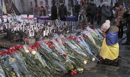 ウクライナの首都キエフで開かれたデモの犠牲者の追悼集会で花をささげて祈る女性＝２０１５年２月２０日（ＡＰ）
