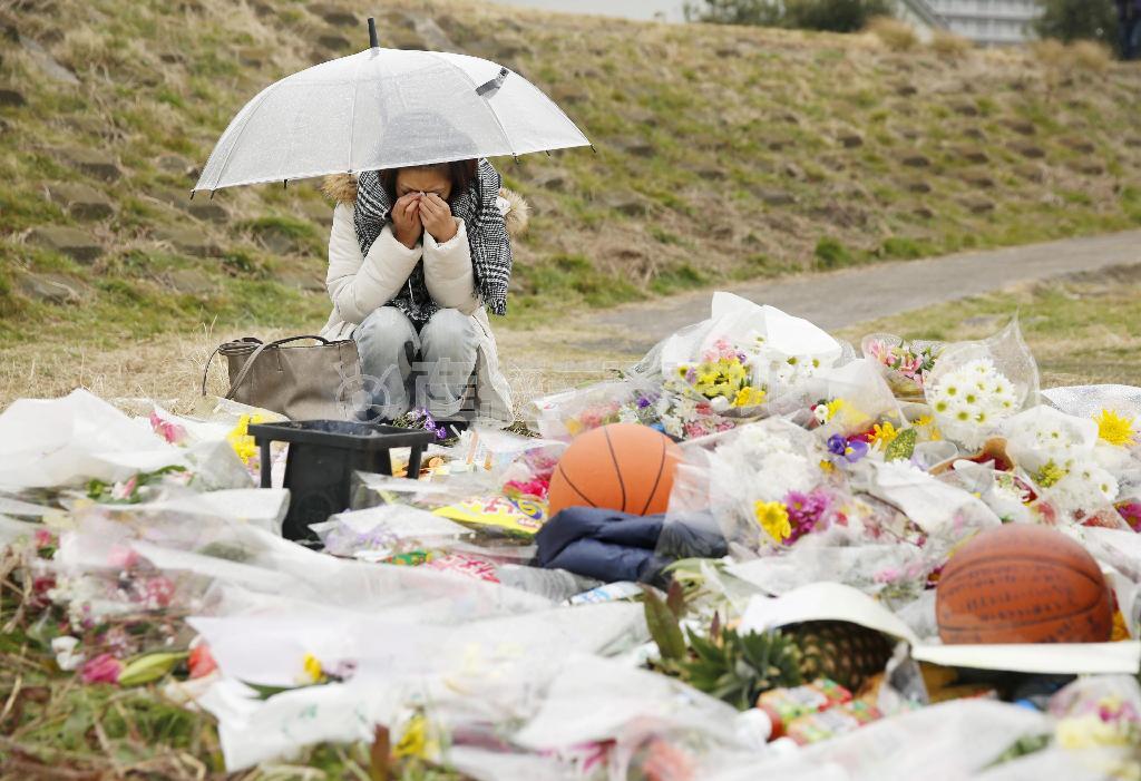 上村（うえむら）遼太さんの遺体が見つかった多摩川河川敷で、花を供え涙ぐむ女性。上村さんへのメッセージが書かれたバスケットボールなども供えられていた＝２０１５年２月２６日午前、神奈川県川崎市川崎区（共同）