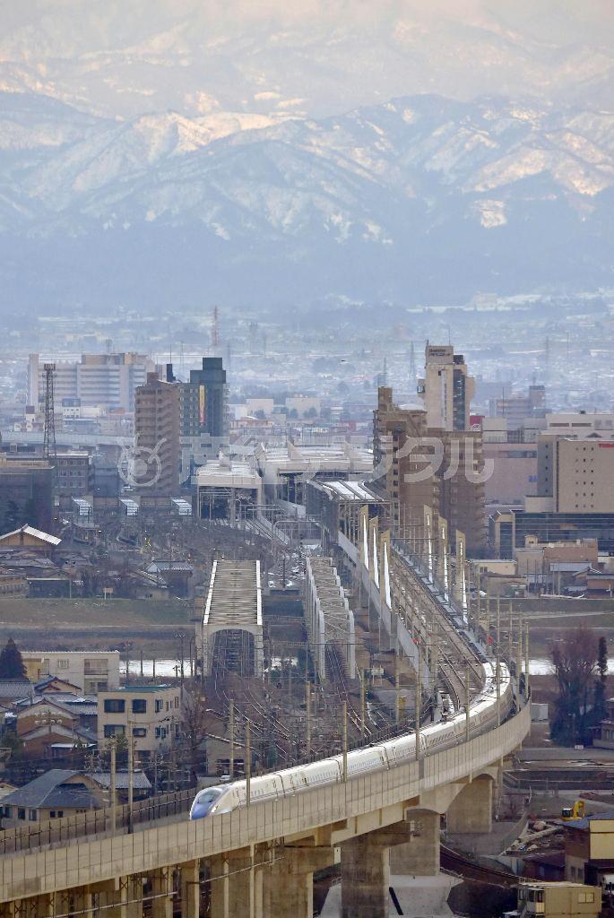 ＪＲ富山駅を出発する北陸新幹線の車両。後方は立山連峰＝富山市