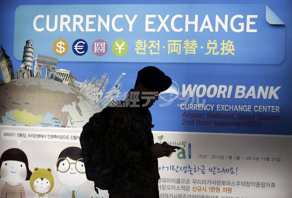 韓国政府がアジアインフラ投資銀行（ＡＩＩＢ）への参加を表明した翌日の３月２７日、首都ソウル市内で外貨両替所のポスターの前を通り過ぎる男性。韓国は経済的利益を優先し、米国の圧力を振り切る形でＡＩＩＢ参加に踏み切った＝２０１５年３月２７日、韓国（ＡＰ）