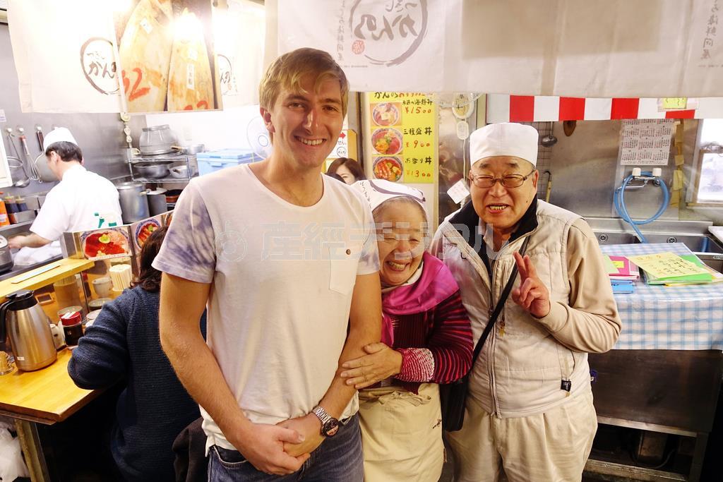 １月の築地です。冬の一番寒い時期に、カナダからやってきたという観光客が半袖で歩いているのを見て、驚いているどんぶり屋のご夫妻。３人を一緒に撮影させてもらいました。背の高い金髪の欧米人と日本のお年寄りの組み合わせは抜群に面白い被写体で、フォトジェニックだと思います＝２０１４年、東京都中央区（須藤夕子さん撮影）