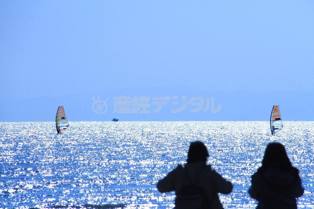 【読者写真（今回の読者：神奈川県鎌倉市、小田扶抄江さん）】きらめく海を背景に、カップルの微妙な距離感が「爽やかさ」を生み出しています。シャッタースピードを早くしているので、ウィンドサーフィンの帆がまったくブレていません。アドバイスをするならば、カップルのお尻くらいまで人物を入れた方が落ち着く構図になるかと思います（提供写真）