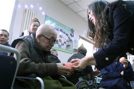 天津市にある老人ホームを訪問し、高齢者にリンゴを手渡す女性。高齢化が急速に進む中国で、老後の生活資金に関心を持つ若者は徐々に増えている（中国新聞社）