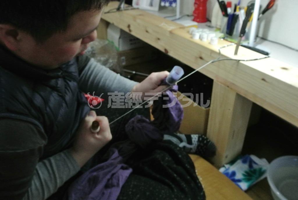 芯を入れて麻糸で縛る田端和樹さん。全体重をかけて縛ることで、しっかりとした防染ができる＝２０１５年３月２４日（提供写真）