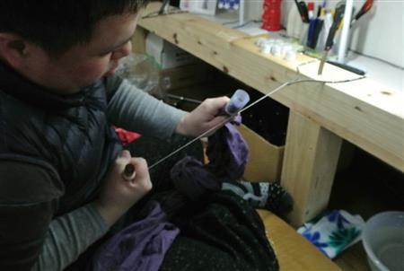 芯を入れて麻糸で縛る田端和樹さん。全体重をかけて縛ることで、しっかりとした防染ができる＝２０１５年３月２４日（提供写真）