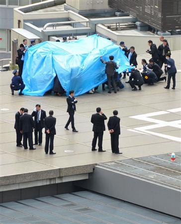 首相官邸の屋上で見つかった無人小型機「ドローン」をシートで覆って調べる捜査員ら＝２２日午前１１時５８分