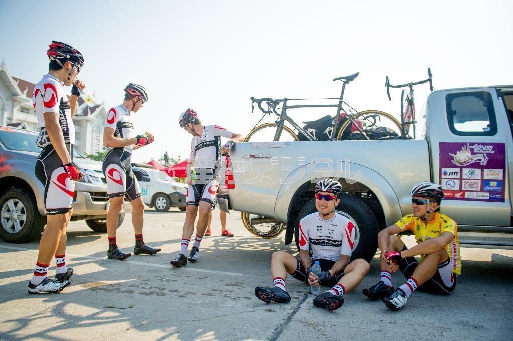 スタート前、車両の陰に座って暑さをしのぐブリヂストンアンカーの選手たち。朝から気温は３０度を超す＝２０１５年４月１日、タイ（田中苑子さん撮影）