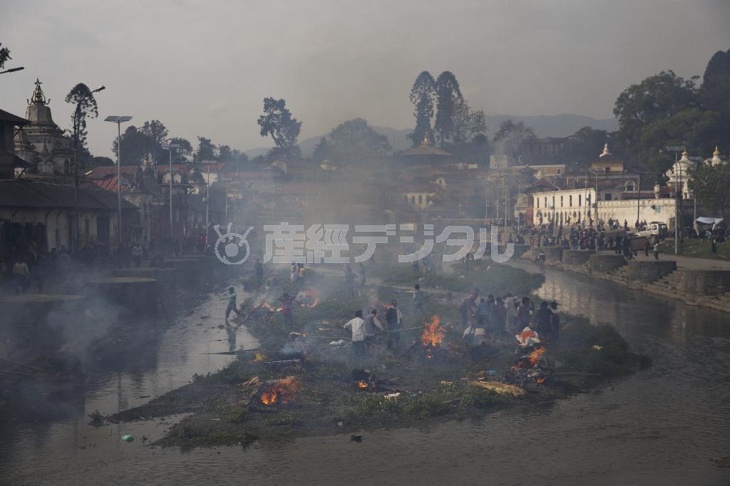 首都カトマンズ市内を流れるバグマティ川の中州で、大地震による犠牲者の遺体を火葬する人々。炎と煙があがる中、読経の声が響いた＝２０１５年４月２６日、ネパール（ＡＰ）