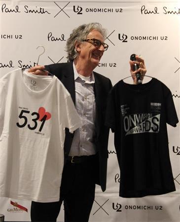 コラボレーション製品の発表会で、Ｔシャツを手に説明するポール・スミス氏。右がインディゴプリントＴシャツ（Ｓ、Ｍ、Ｌ、いずれも９７２０円）、左がオーガニックコットンプリントＴシャツ（Ｓ、Ｍ、Ｌ、いずれも７５６０円）＝２０１５年４月１０日、広島県尾道市（田中幸美撮影）