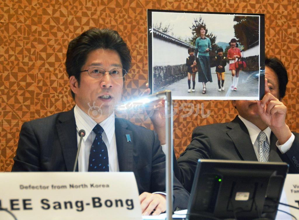 ５月５日、米ニューヨークで開かれた国際シンポジウムで、拉致被害者の横田めぐみさんと一緒に納まった写真を示しながらスピーチする横田拓也さん（左）＝２０１５年（共同）